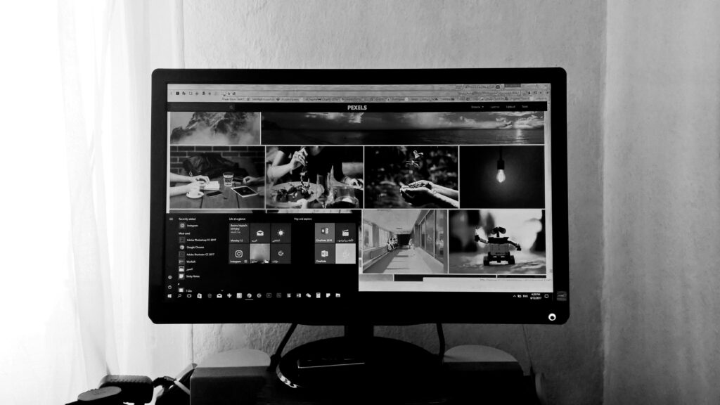 A black and white photo of a computer monitor displaying various images and applications in an indoor setting.