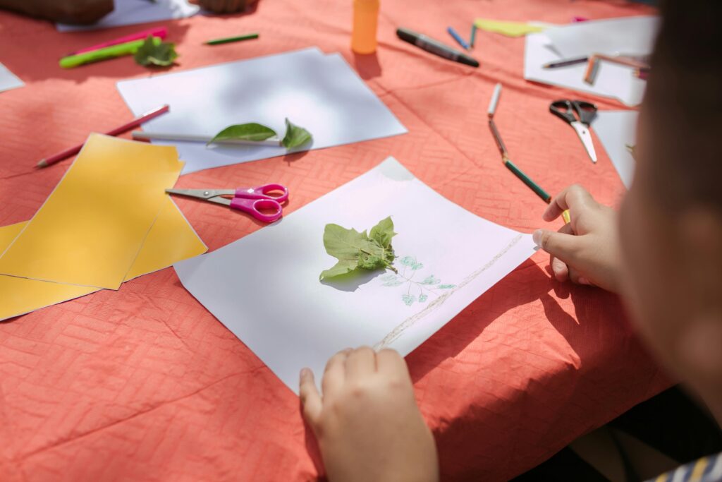 Hands crafting with paper and leaves at a colorful art table.